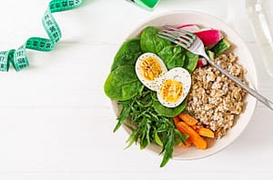 Assiette équilibrée et colorée avec oeufs, épinards, salade, carottes, radis et céréales.